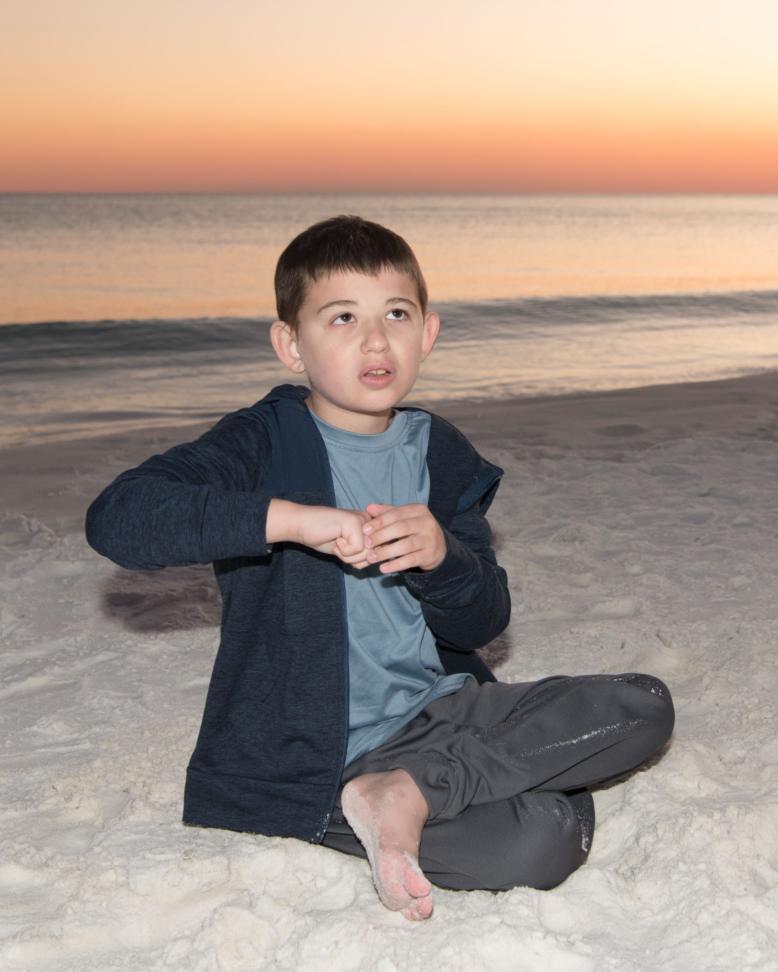 Luke sitting on the beach watching the beautiful sunset with sand between his toes.